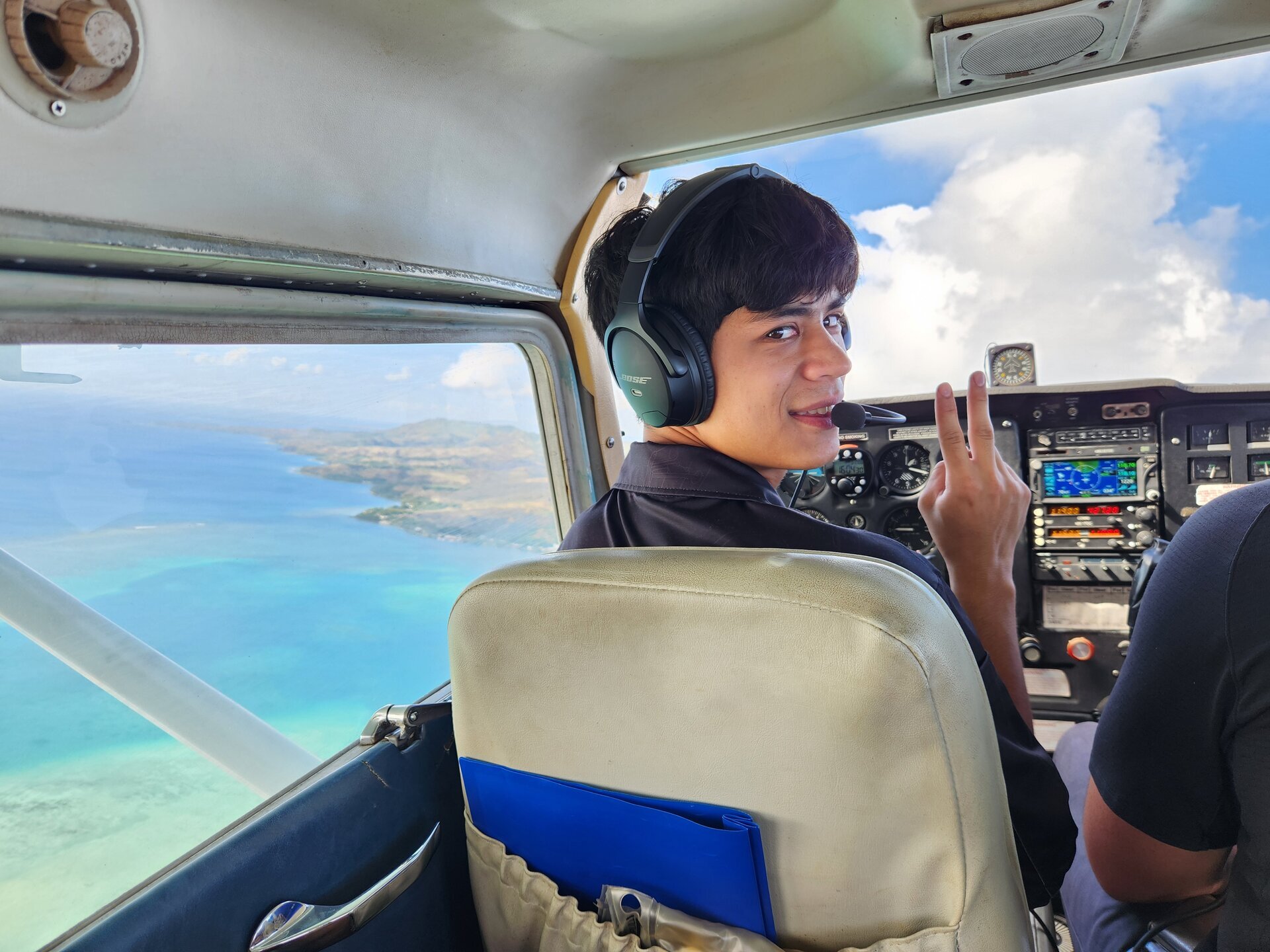 Jaden Goode smiling in cockpit, headset on, turquoise ocean visible through window