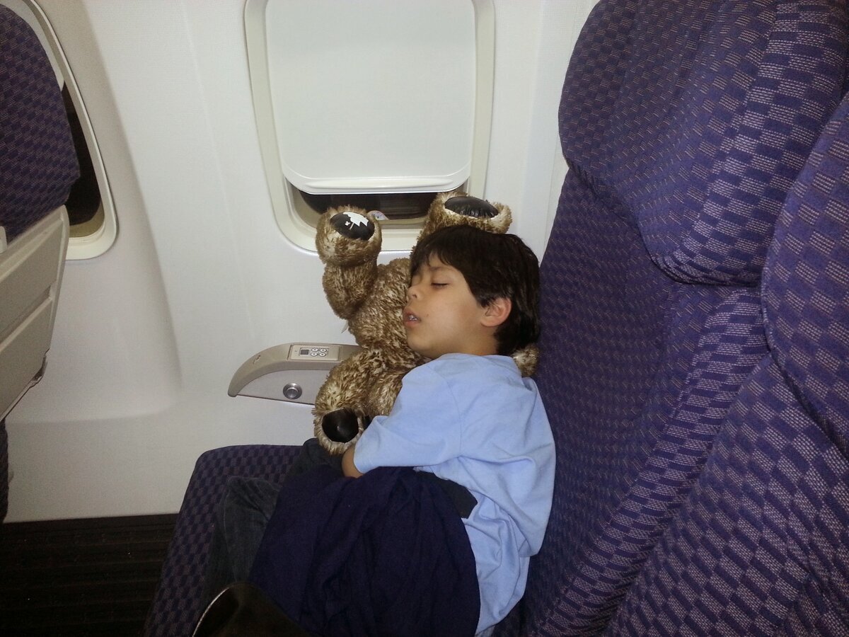 Young Jaden sleeping on airplane seat with teddy bear